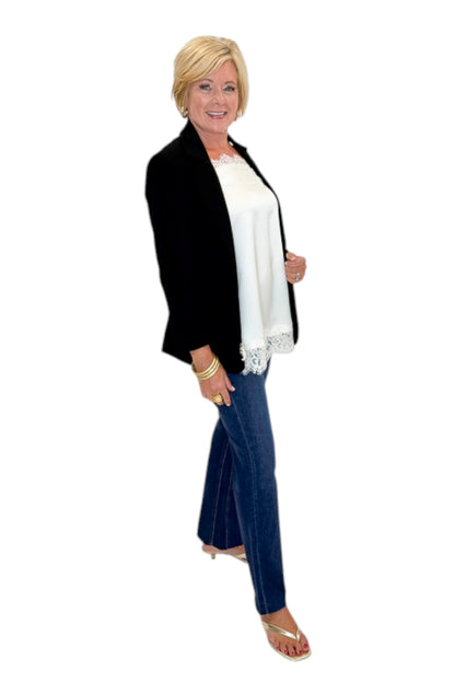 Side view of woman wearing Swagger Boutique’s Black Blazer and Ivory Satin Lace Trim Tank Top by Entro with jeans against white studio background.