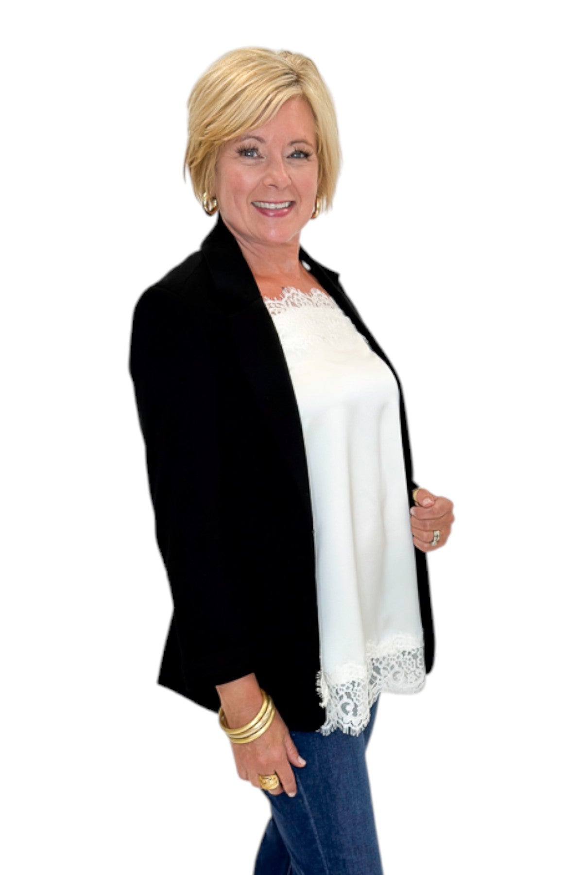 Side view of woman wearing Swagger Boutique’s Black Blazer and Ivory Satin Lace Trim Tank Top by Entro with jeans against white studio background.