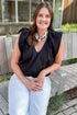 Front view of woman wearing Swagger Boutique’s Black Bubble Hem Pleated Top with jeans sitting outside on a bench.