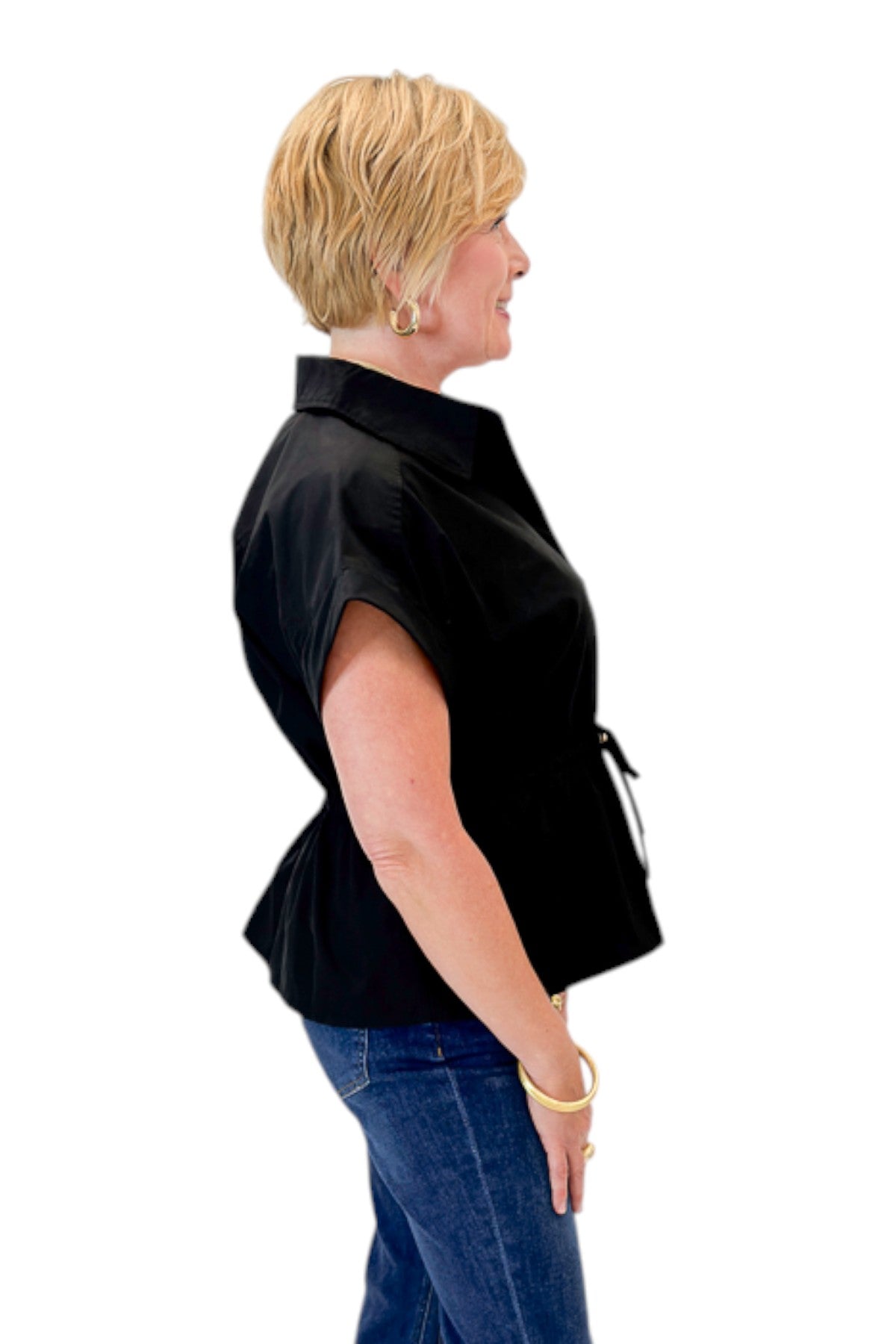 Side view of woman wearing Swagger Boutique’s Black Cinched Waist Short Sleeve Top by Entro with jeans against white studio background.