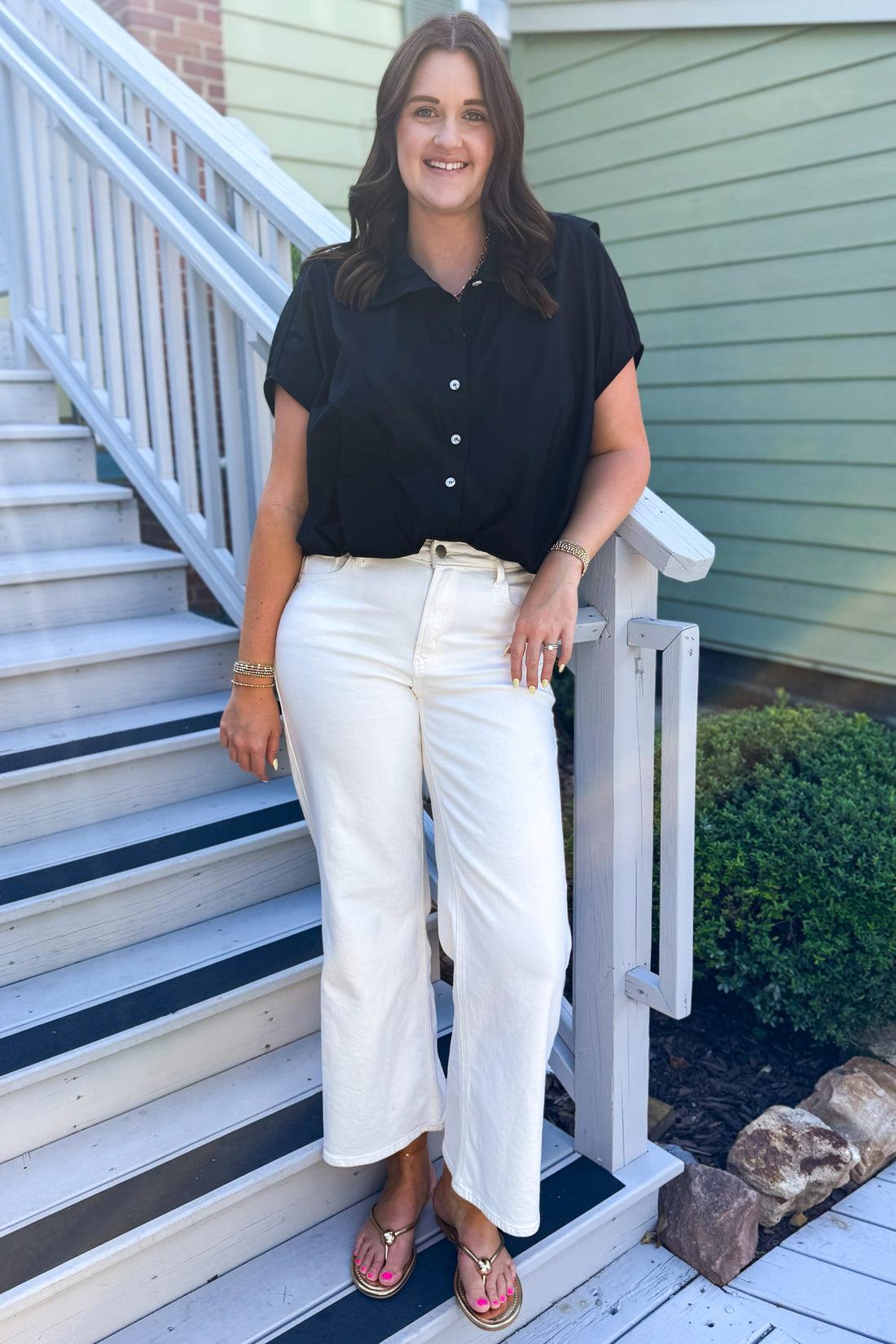 Front view of woman wearing Swagger Boutique’s Black Collared Bubble Hem Top with jeans standing outside by stairs.