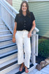 Front view of woman wearing Swagger Boutique’s Black Collared Bubble Hem Top with jeans standing outside by stairs.