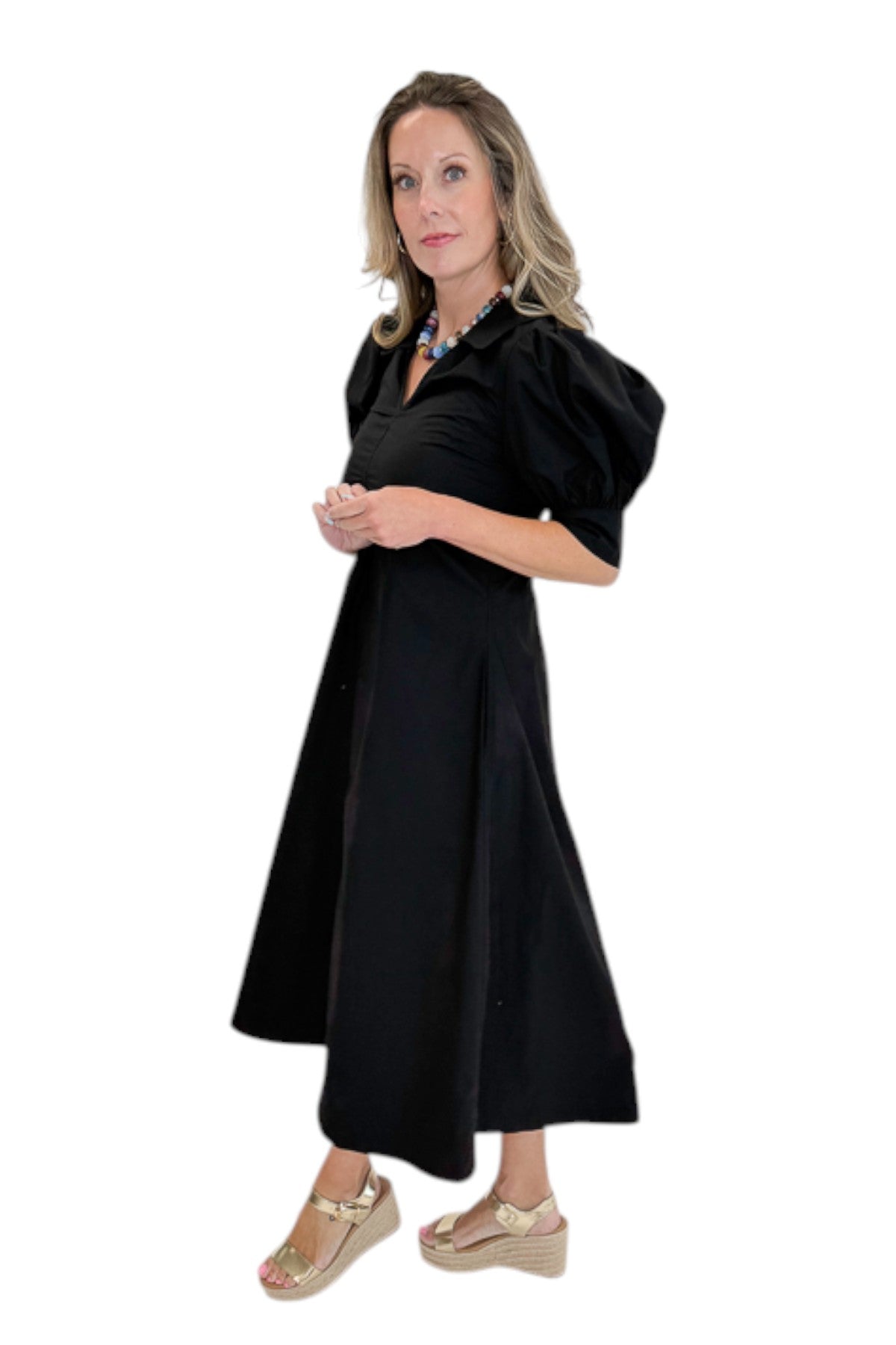 Side view of woman wearing Swagger Boutique’s Black Collared Midi Dress with sandals against white studio background.