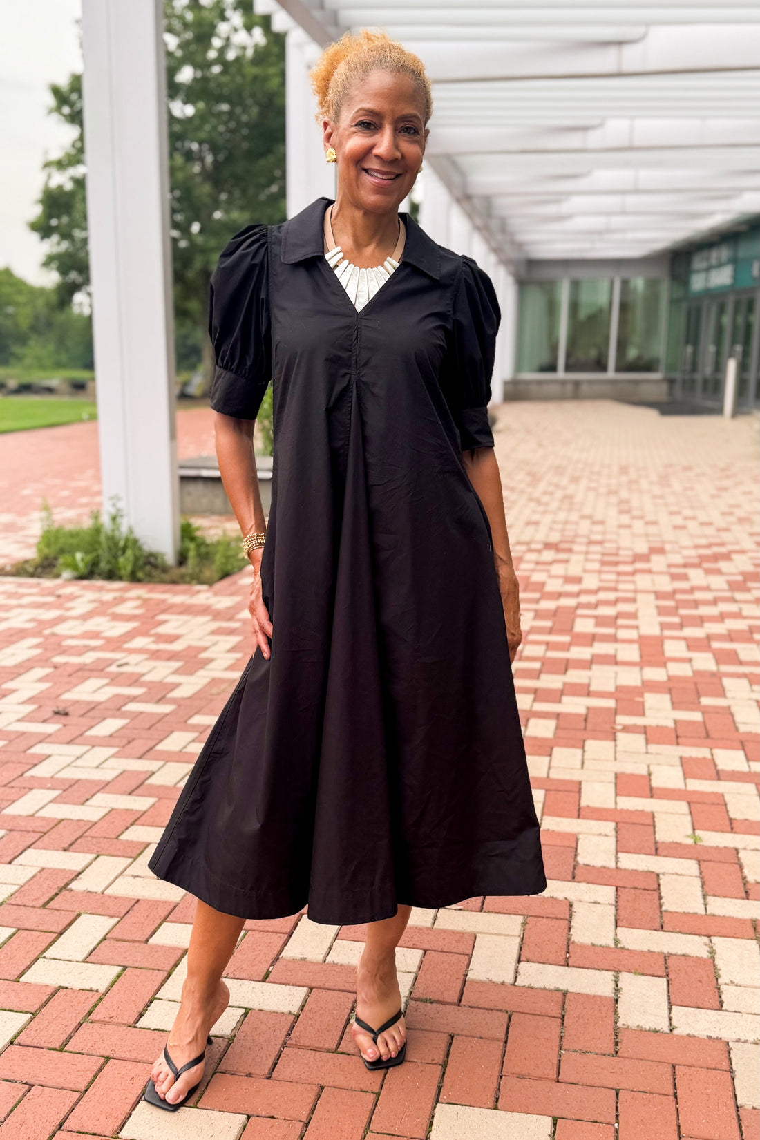 Front view of woman wearing Swagger Boutique’s Black Collared Midi Dress outside by a red brick walkway.