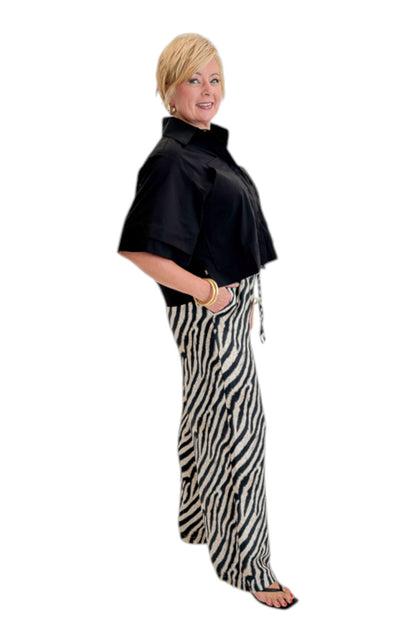 Side view of woman wearing Swagger Boutique’s Black Collared Short Sleeve Top with Zebra Wide Leg Pants by Entro against white studio background.