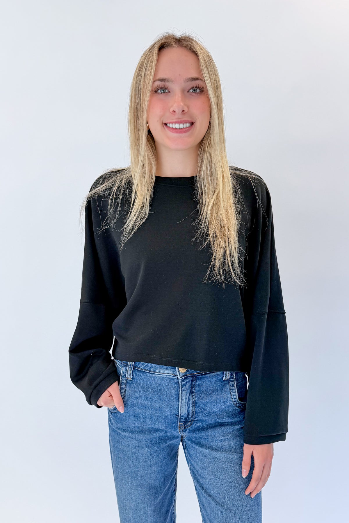 Front view of woman wearing Swagger Boutique’s black cropped sweatshirt with jeans against white studio background.