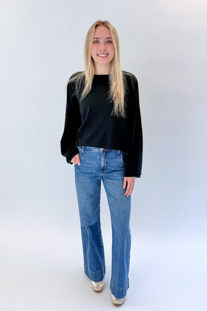 Front view of woman wearing Swagger Boutique’s black cropped sweatshirt with jeans against white studio background.