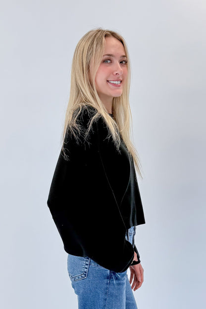 Side view of woman wearing Swagger Boutique’s black cropped sweatshirt with jeans against white studio background.