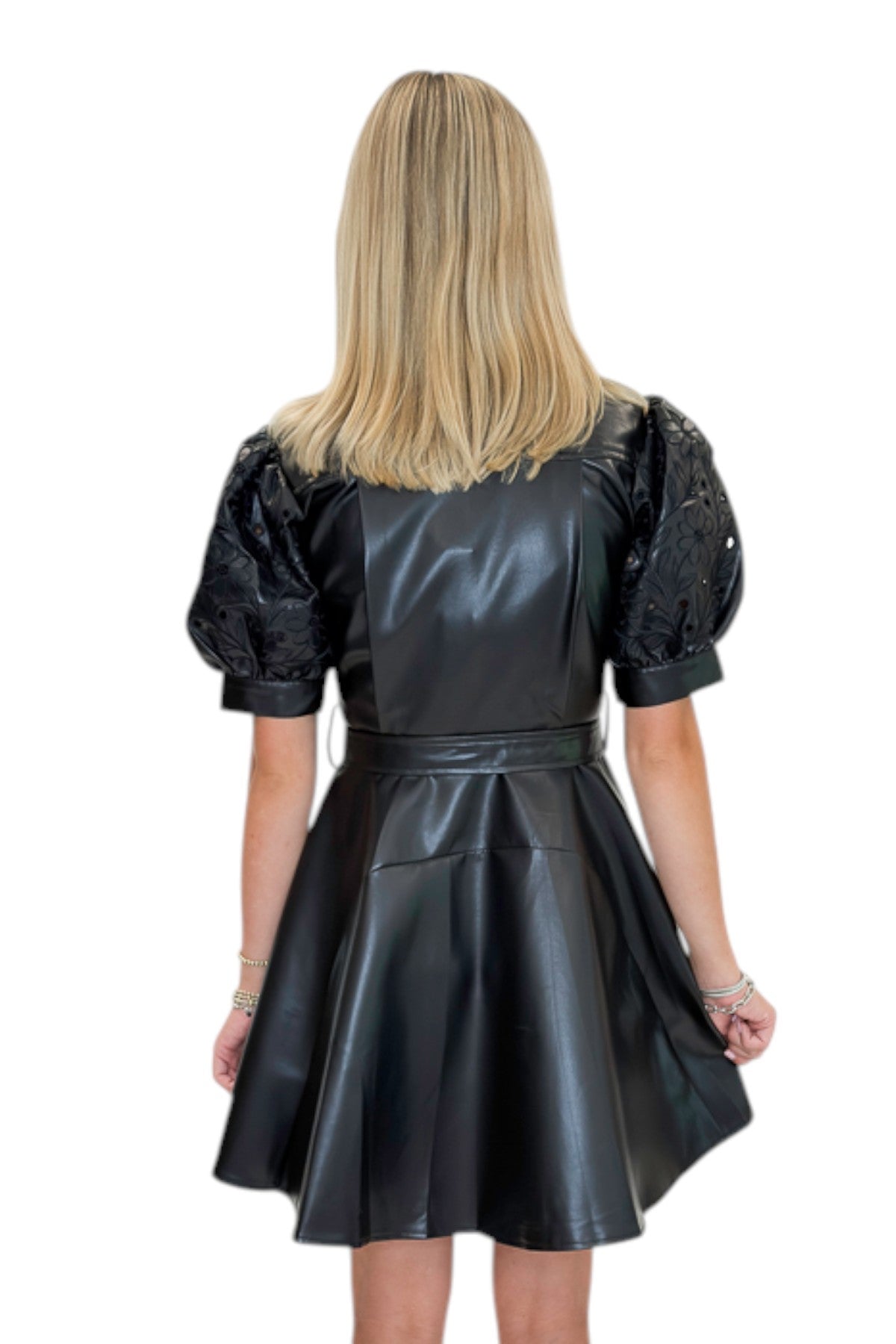 Back view of woman wearing Swagger Boutique’s Black Embroidered Faux Leather Dress with heels against white studio background.