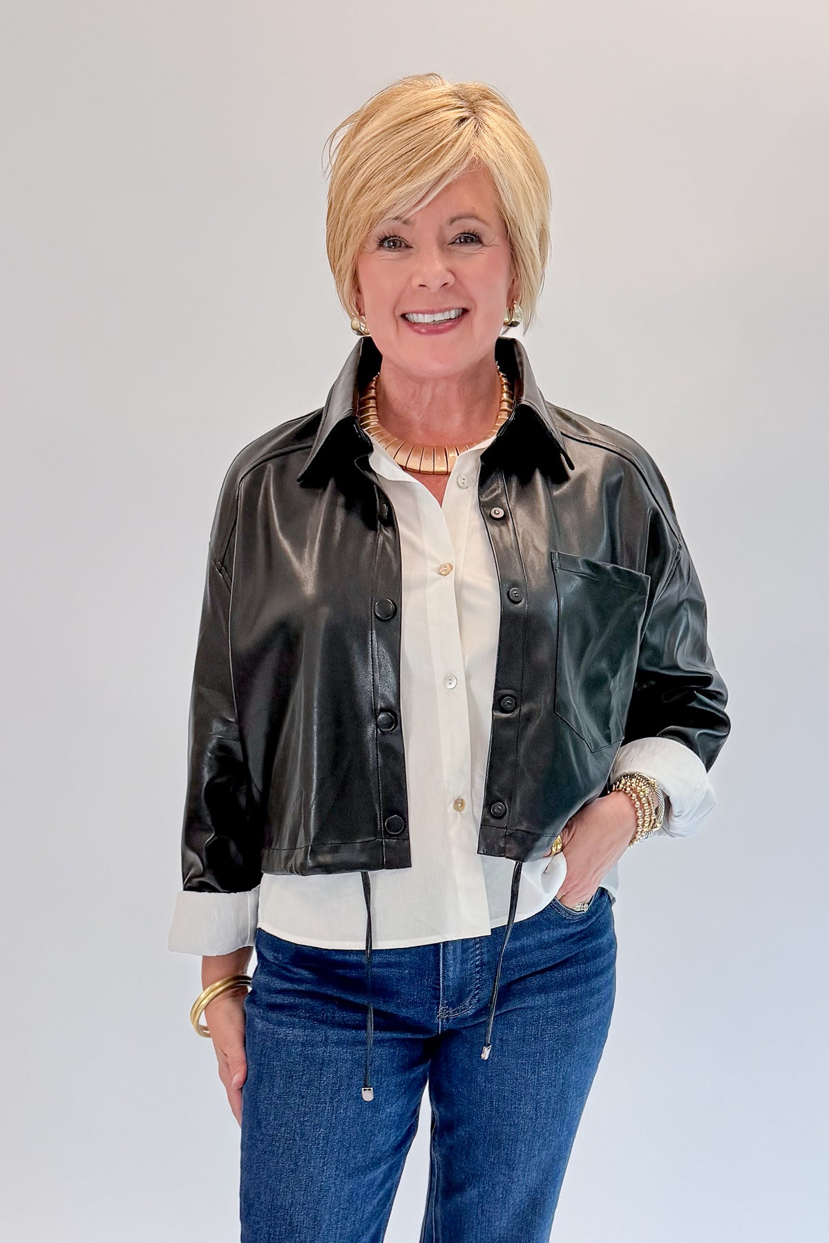 Front view of woman wearing Swagger Boutique’s Black Faux Leather Jacket With Layered Shirt with jeans against white studio background.
