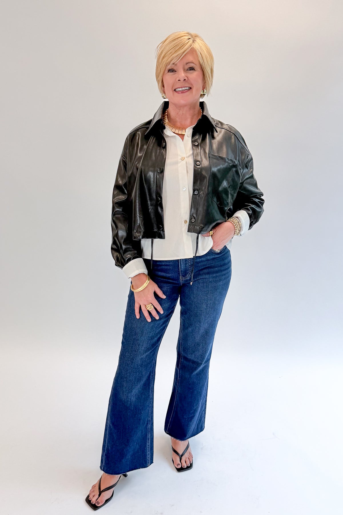 Front view of woman wearing Swagger Boutique’s Black Faux Leather Jacket With Layered Shirt with jeans against white studio background.