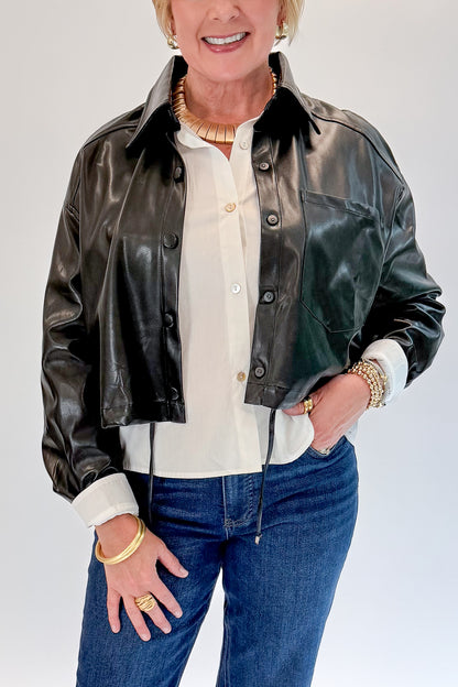 Front detail view of woman wearing Swagger Boutique’s Black Faux Leather Jacket With Layered Shirt with jeans against white studio background.