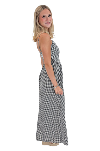 Side view of woman wearing Swagger Boutique’s Black Gingham Maxi Dress with sandals against white studio background.