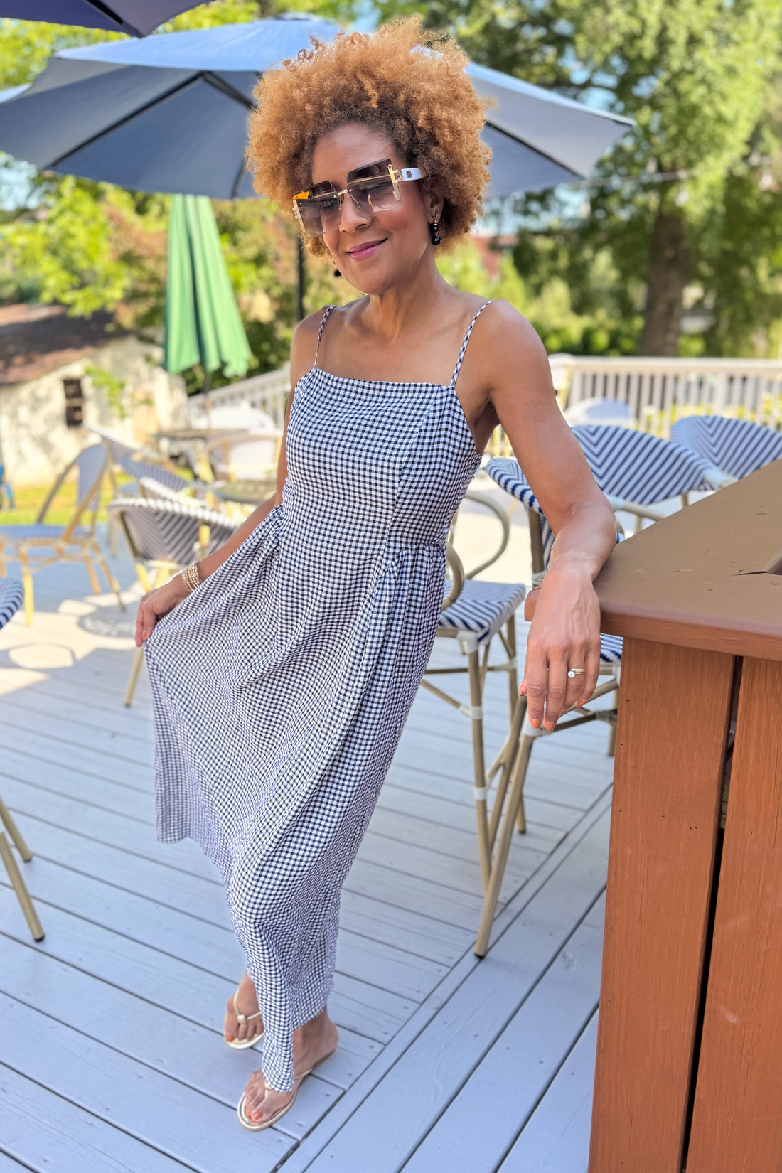 Front view of woman wearing Swagger Boutique’s Black Gingham Maxi Dress with sandals standing outside at a restaurant.