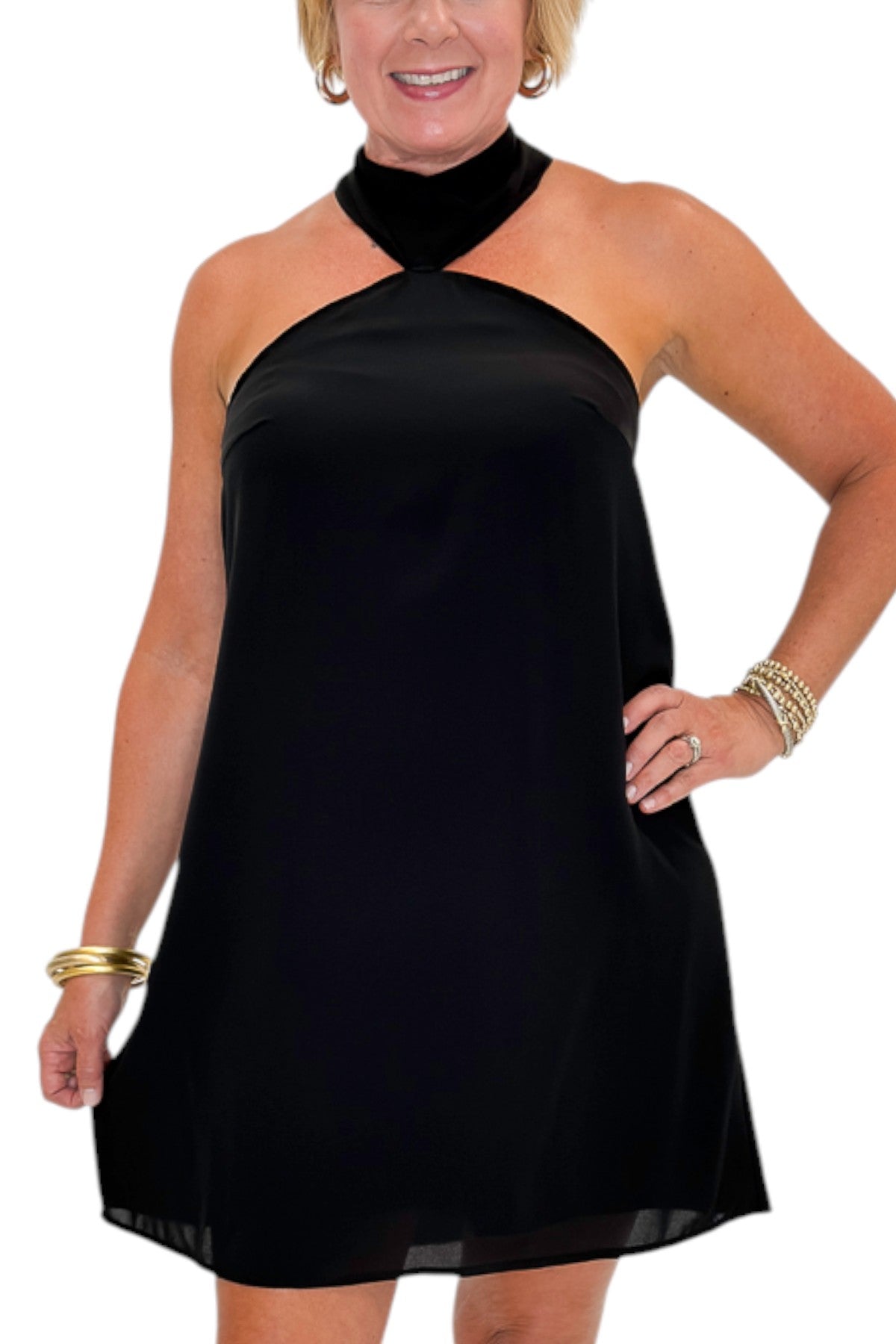 Front detail view of woman wearing Swagger Boutique’s Black Halter Neck Mini Dress with heels against white studio background.