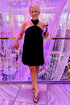 Front view of woman wearing Swagger Boutique’s Black Halter Neck Mini Dress with heels at a fancy restaurant. 