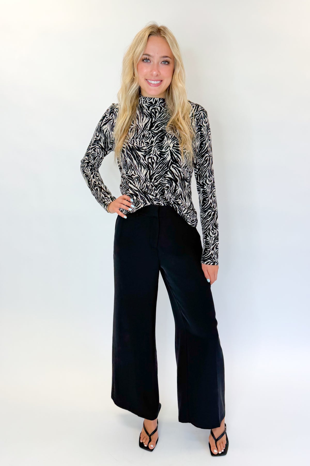 Front view of woman wearing Swagger Boutique’s Black High Waisted Trousers by Skies Are Blue &amp; Zebra Mock Neck Long Sleeve Top by Entro against white studio background.