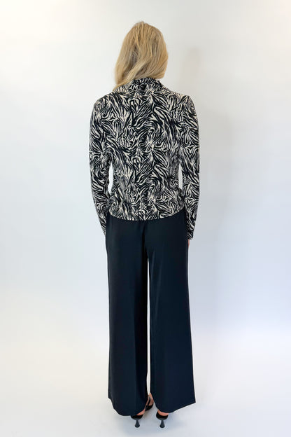 Back view of woman wearing Swagger Boutique’s Black High Waisted Trousers by Skies Are Blue &amp; Zebra Mock Neck Long Sleeve Top by Entro against white studio background.