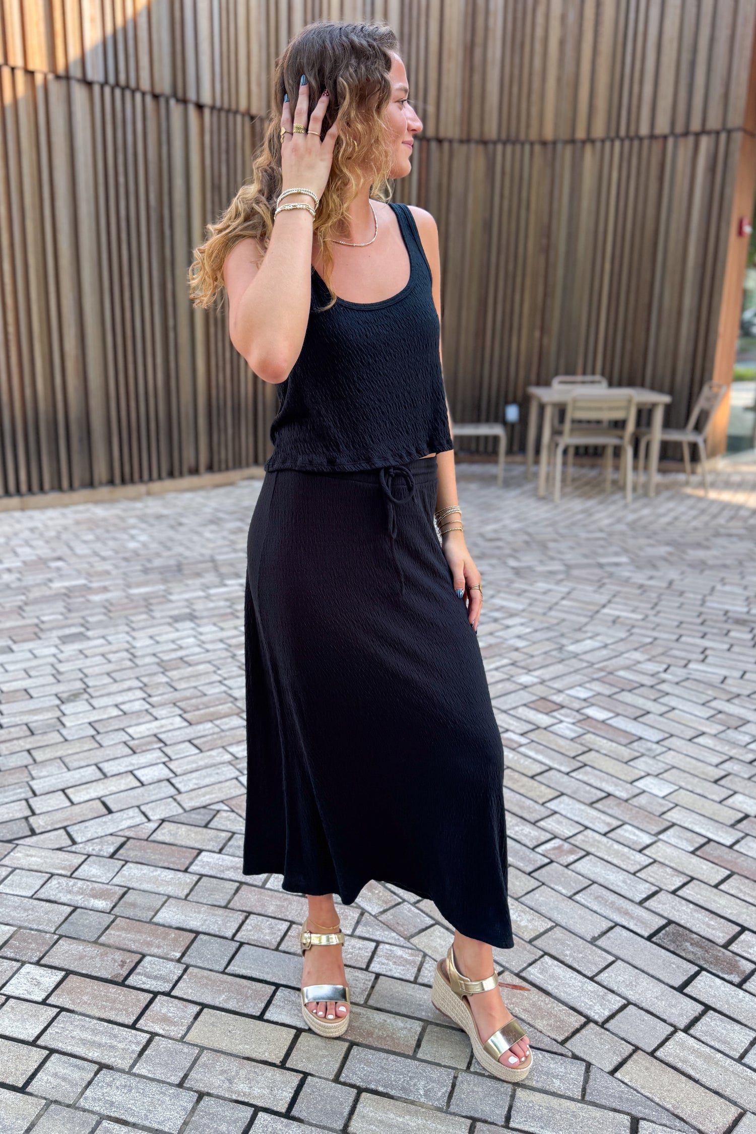 Front view of woman wearing Swagger Boutique’s Black Joanna Tank by Z Supply with Black Idris Maxi Skirt by Z Supply standing outside on a brick pathway.