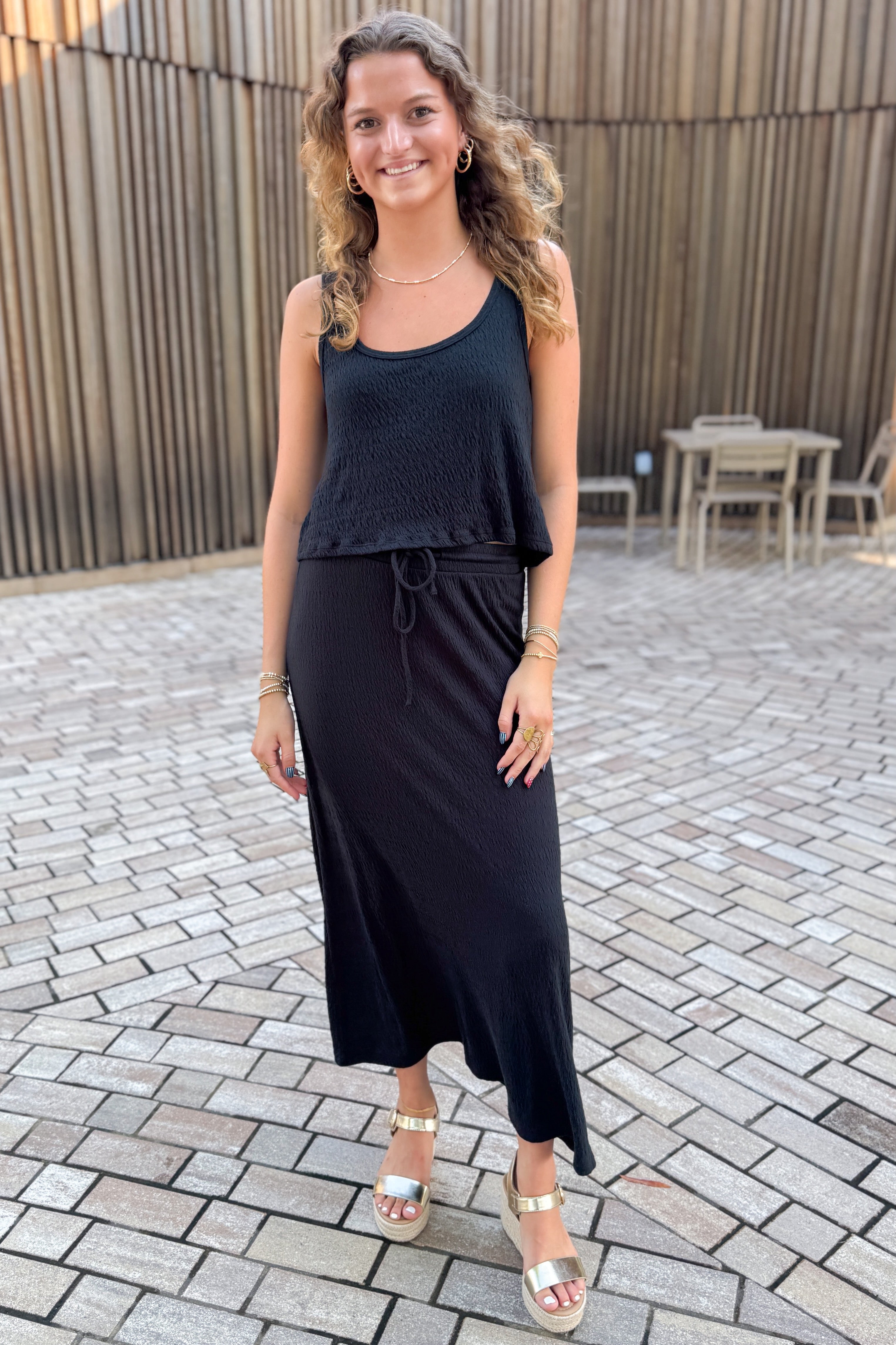 Front view of woman wearing Swagger Boutique’s Black Joanna Tank by Z Supply with Black Idris Maxi Skirt by Z Supply standing outside on a brick pathway.