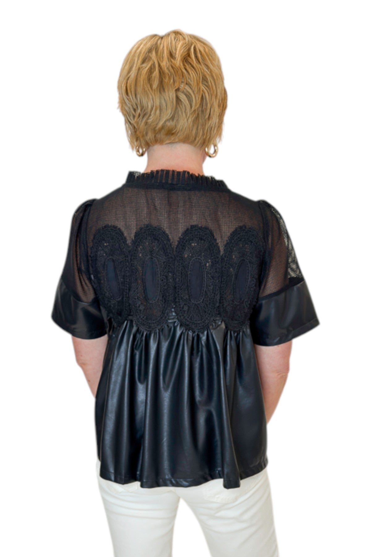 Back view of woman wearing Swagger Boutique’s Black Lace Applique Faux Leather Top with jeans against white studio background.