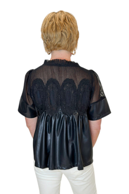 Back view of woman wearing Swagger Boutique’s Black Lace Applique Faux Leather Top with jeans against white studio background.