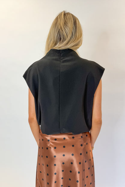 Back view of woman wearing Swagger Boutique’s Camel Polka Dot Satin Skirt with Black Mock Neck Bubble Hem Tank against white studio background.