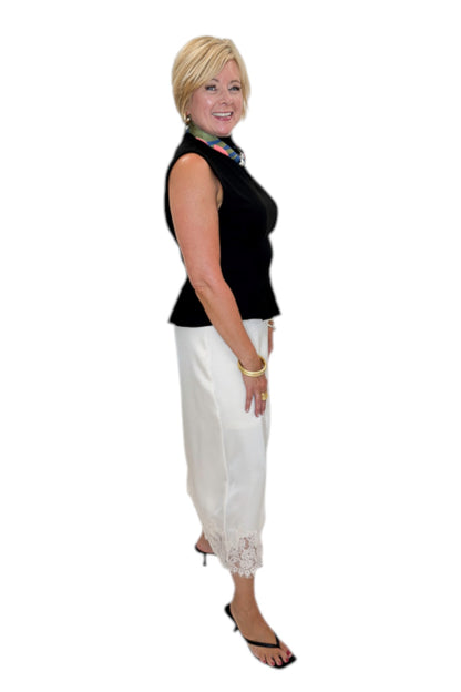 Side view of woman wearing Swagger Boutique’s Black Mock Neck Pleat Waist Top by Entro with skirt against white studio background.