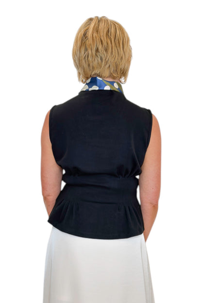 Back view of woman wearing Swagger Boutique’s Black Mock Neck Pleat Waist Top by Entro with skirt against white studio background.
