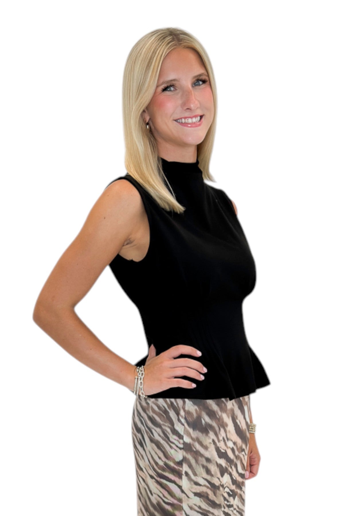 Side view of woman wearing Swagger Boutique’s Black Mock Neck Pleat Waist Top by Entro with skirt against white studio background.