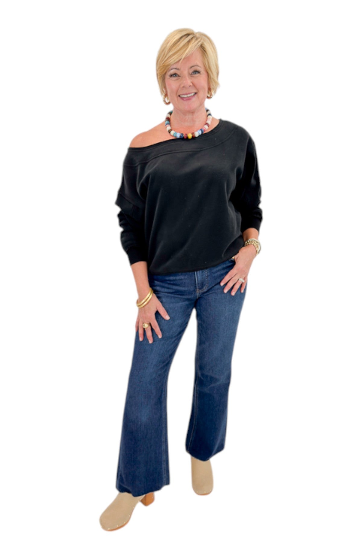 Front view of woman wearing Swagger Boutique’s Black Off The Shoulder Sweatshirt with jeans against white studio background.