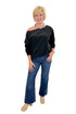 Front view of woman wearing Swagger Boutique’s Black Off The Shoulder Sweatshirt with jeans against white studio background.