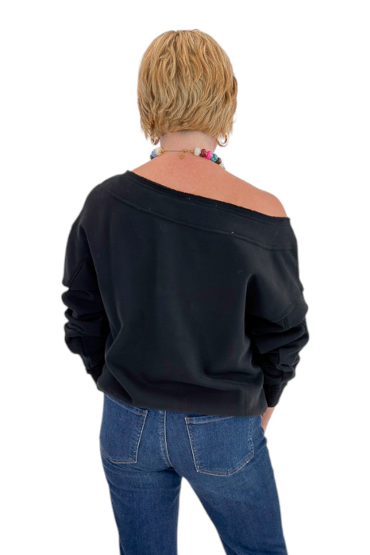 Back view of woman wearing Swagger Boutique’s Black Off The Shoulder Sweatshirt with jeans against white studio background.
