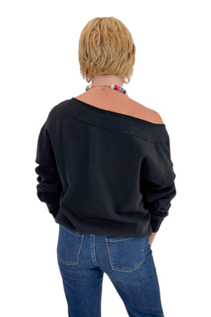 Back view of woman wearing Swagger Boutique’s Black Off The Shoulder Sweatshirt with jeans against white studio background.