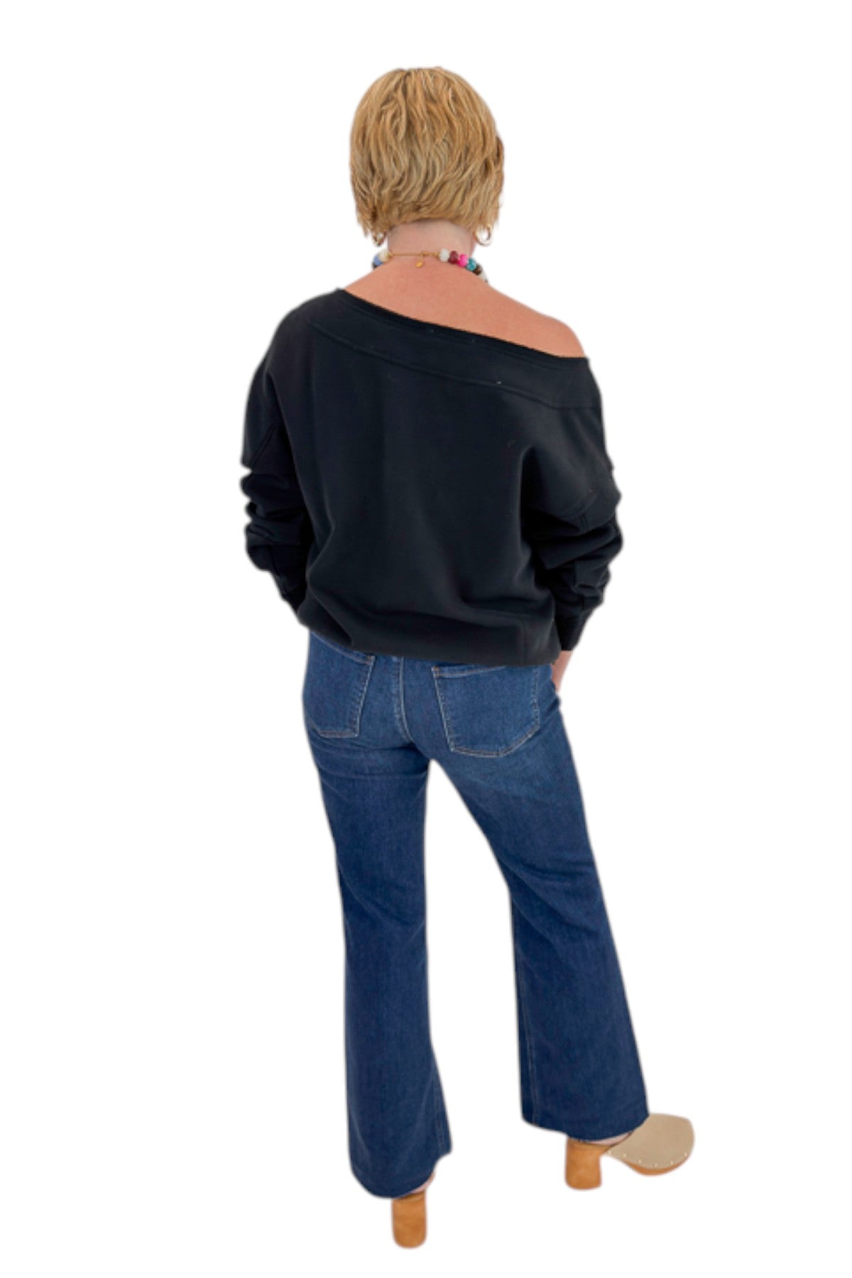 Back view of woman wearing Swagger Boutique’s Black Off The Shoulder Sweatshirt with jeans against white studio background.