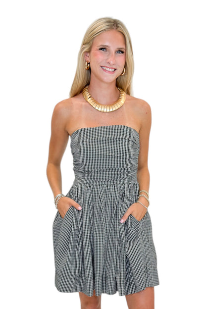 Front view of woman wearing Swagger Boutique’s Black Plaid Strapless Mini Dress with boots against white studio background.