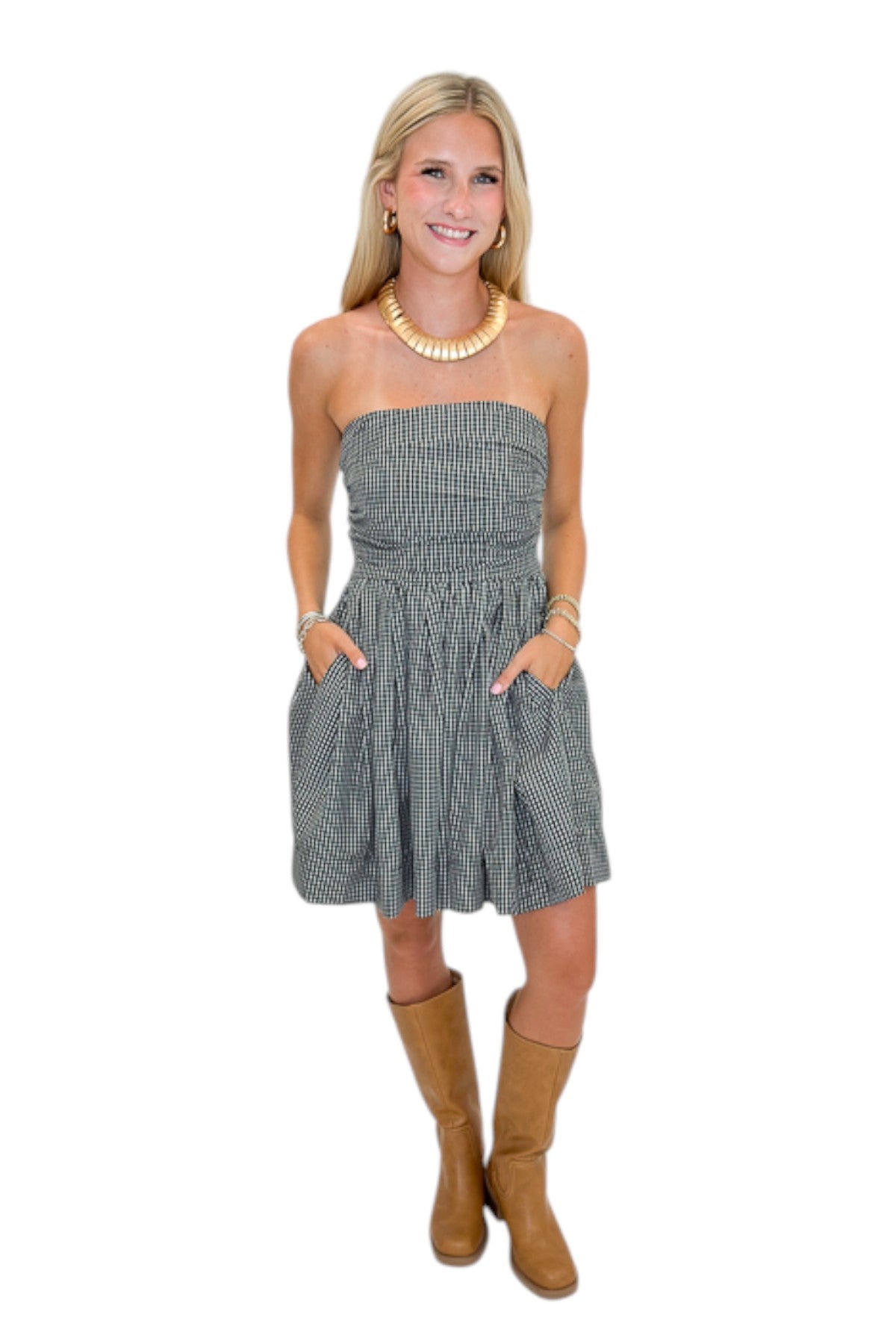 Front view of woman wearing Swagger Boutique’s Black Plaid Strapless Mini Dress with boots against white studio background.