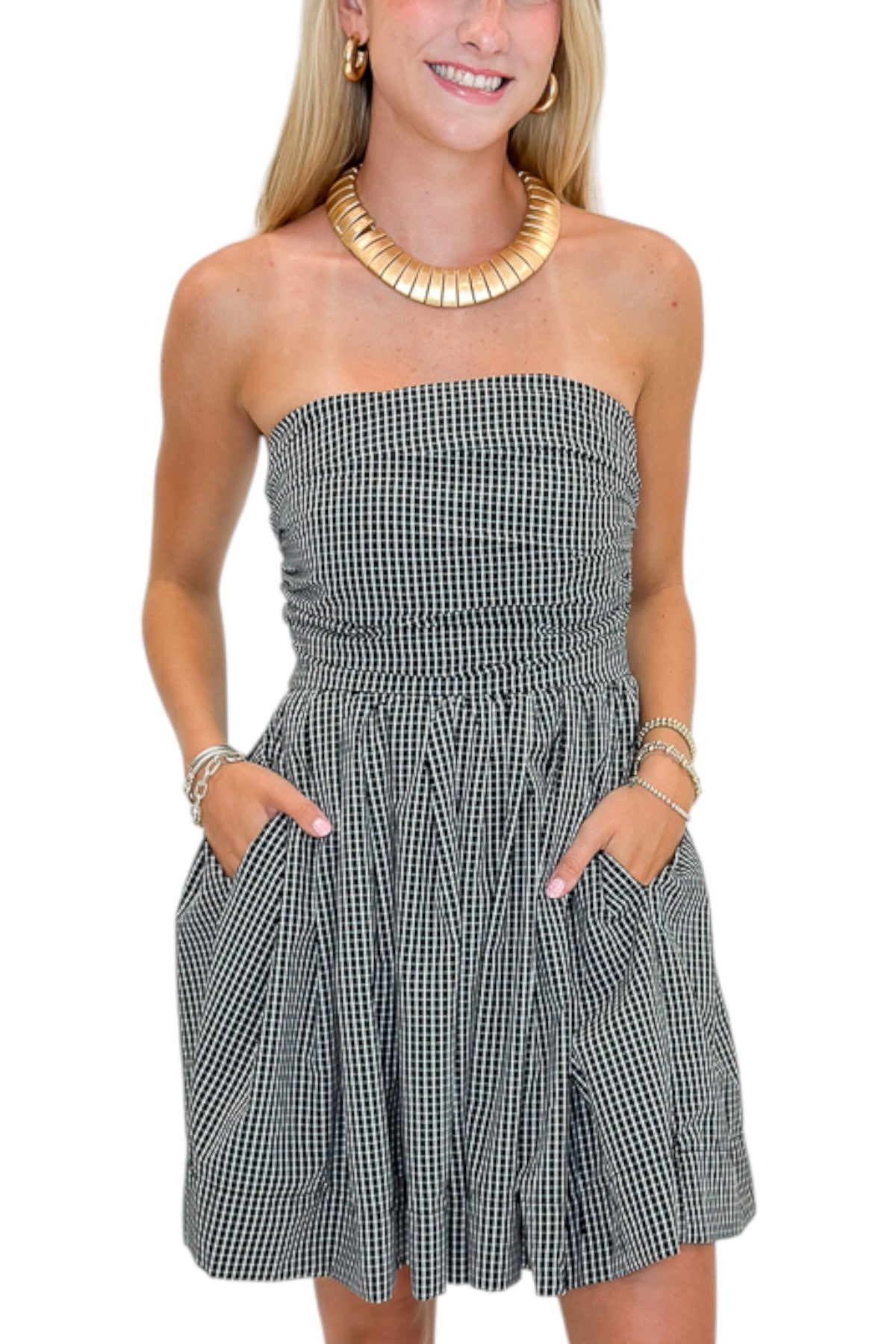 Front detail view of woman wearing Swagger Boutique’s Black Plaid Strapless Mini Dress with boots against white studio background.