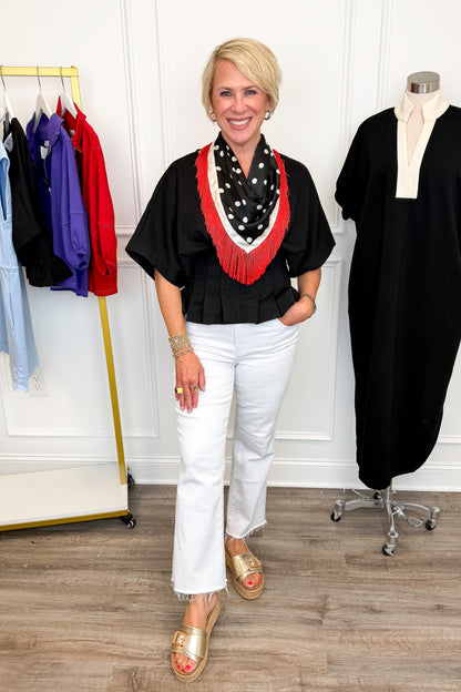 Front view of woman wearing Swagger Boutique’s Black Pleat Detail Dolman Sleeve Top with jeans with clothing hanging in the background.