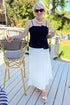 Front view of woman wearing Swagger Boutique’s Black Pleat Detail Tank and white skirt at an outdoor patio.
