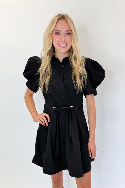 Front view of woman wearing Swagger Boutique’s Black Puff Sleeve Mini Dress by Entro against white studio background.