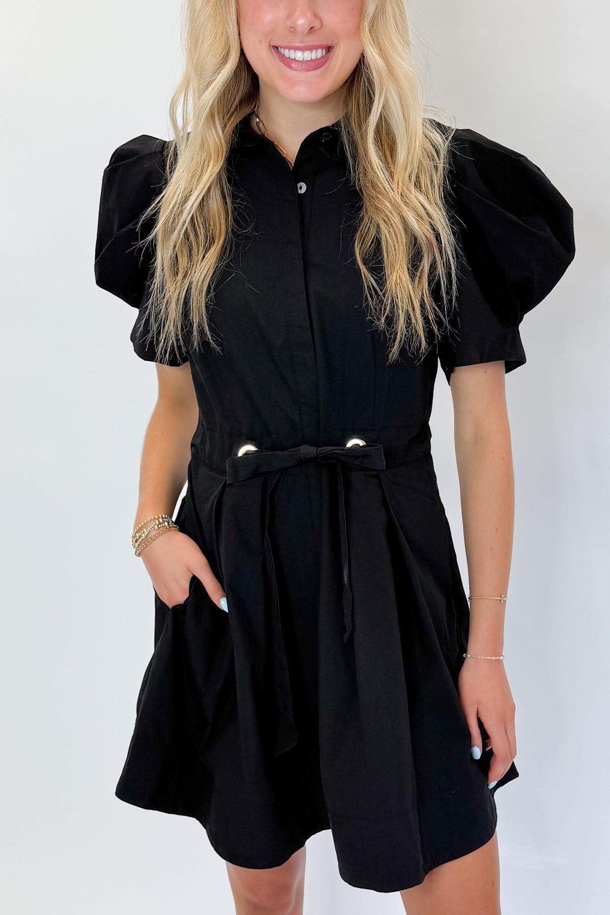 Front detail view of woman wearing Swagger Boutique’s Black Puff Sleeve Mini Dress by Entro against white studio background.