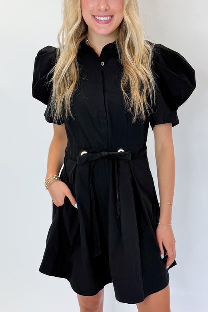 Front detail view of woman wearing Swagger Boutique’s Black Puff Sleeve Mini Dress by Entro against white studio background.