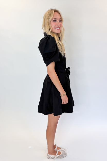 Side view of woman wearing Swagger Boutique’s Black Puff Sleeve Mini Dress by Entro against white studio background.