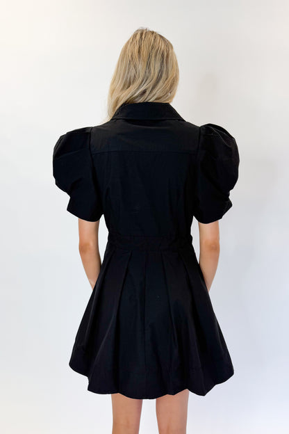 Back view of woman wearing Swagger Boutique’s Black Puff Sleeve Mini Dress by Entro against white studio background.