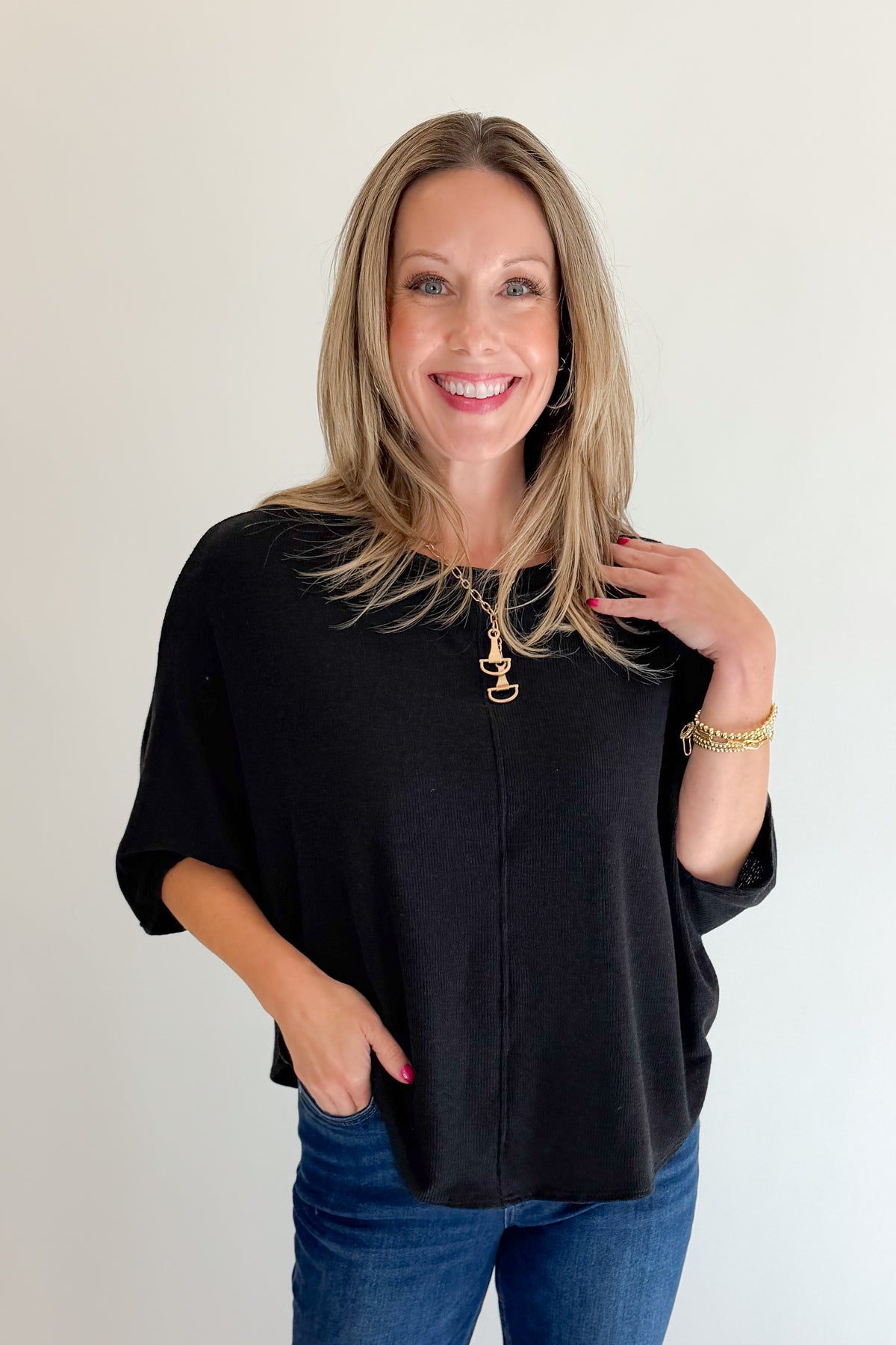 Front view of woman wearing Swagger Boutique’s Black Ribbed Dolman Sleeve Top with jeans against white studio background.