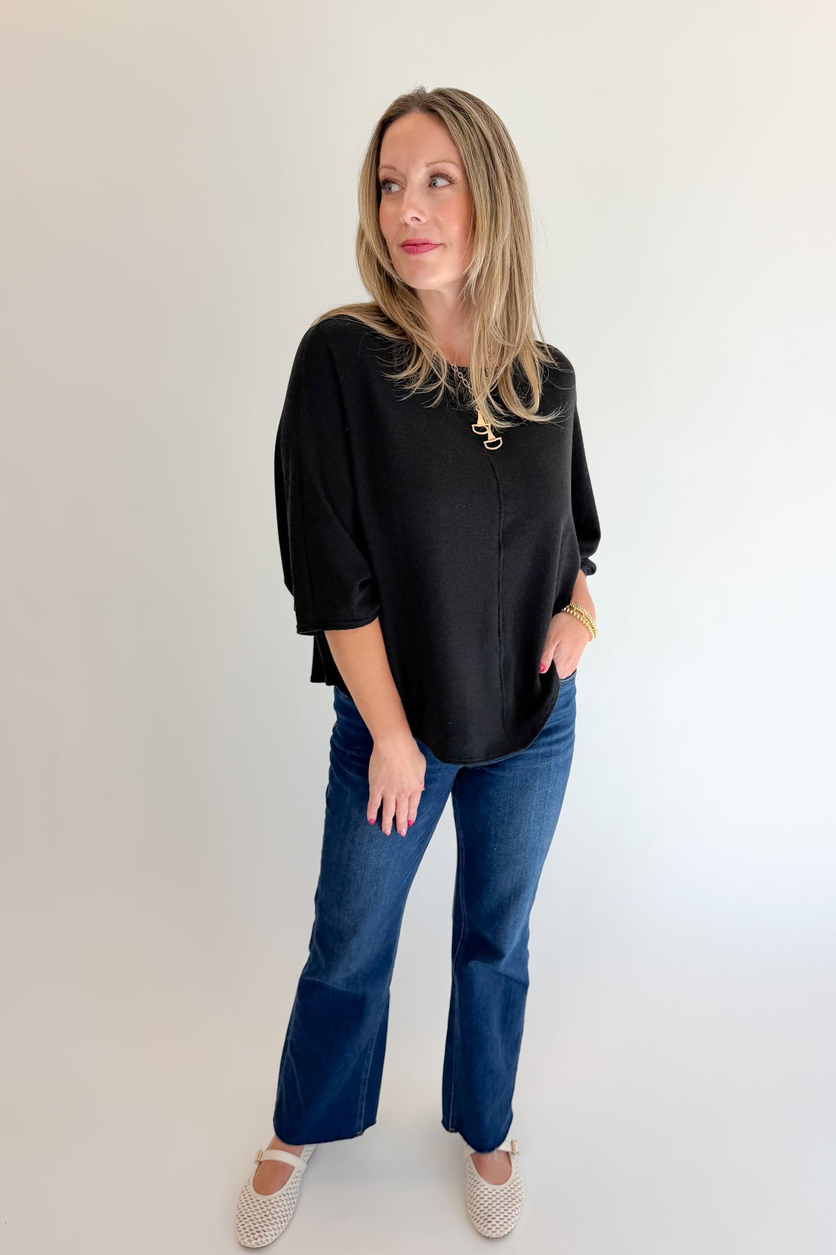 Front view of woman wearing Swagger Boutique’s Black Ribbed Dolman Sleeve Top with jeans against white studio background.