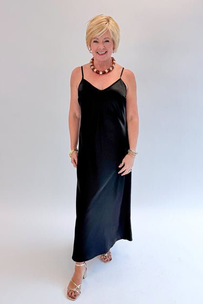 Front view of woman wearing Swagger Boutique’s Black Satin Dress with heels against white studio background.