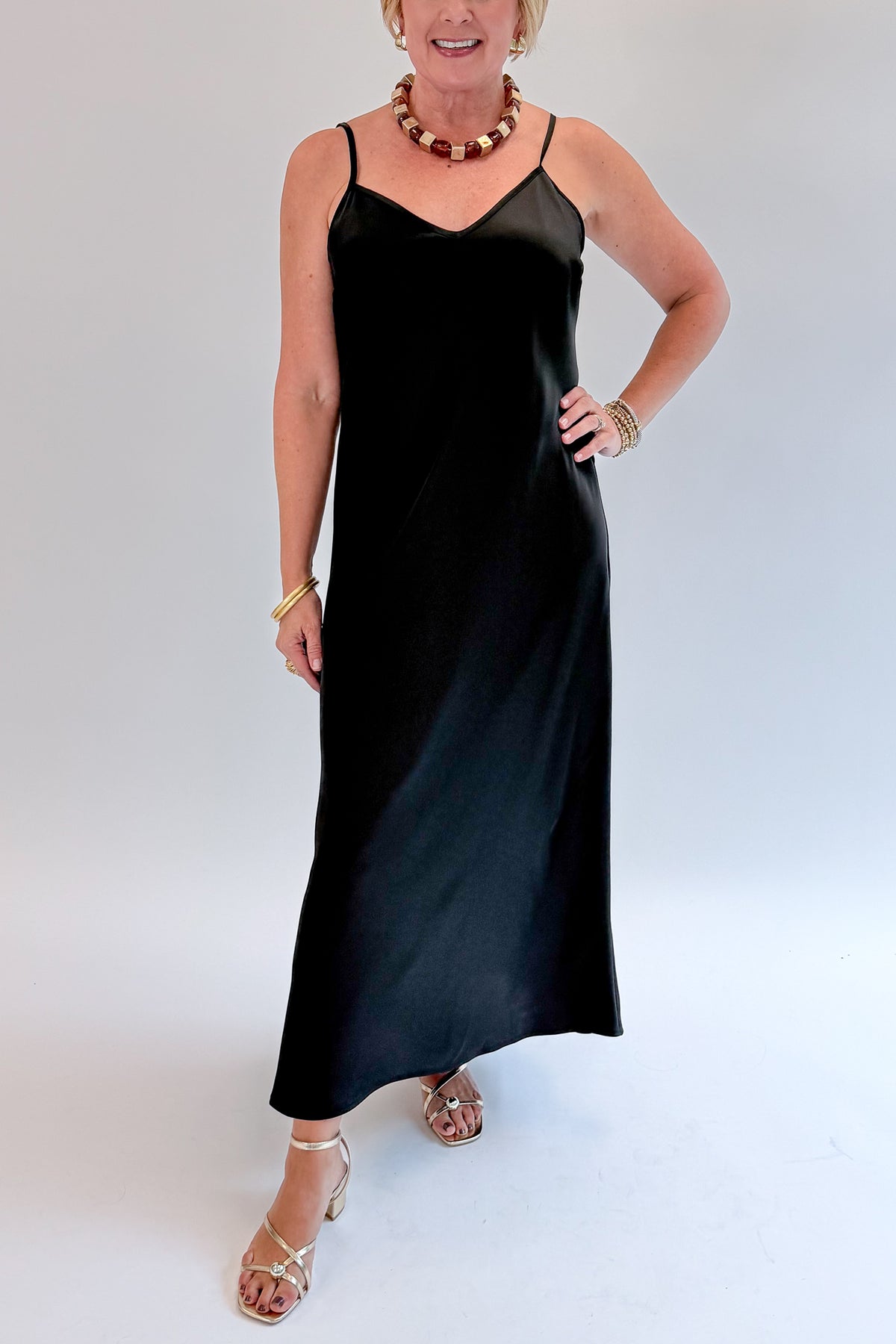 Front detail view of woman wearing Swagger Boutique’s Black Satin Dress with heels against white studio background.