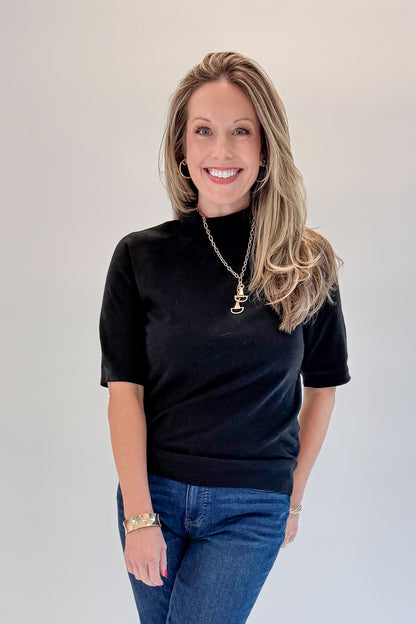 Front view of woman wearing Swagger Boutique’s Black Short Sleeve Turtleneck Sweater with jeans against white studio background.